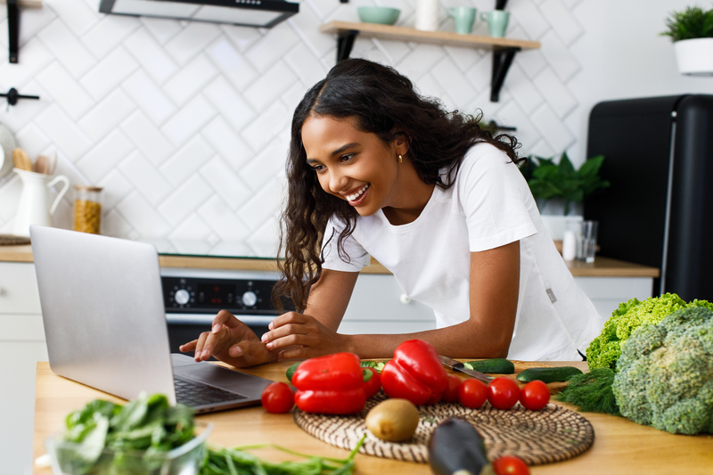 young woman in kitchen looking at a laptop screen